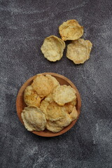 Emping, Indonesian traditional snack made from melinjo or belinjo seeds. Bitter and savory. served on wooden plate with black background
