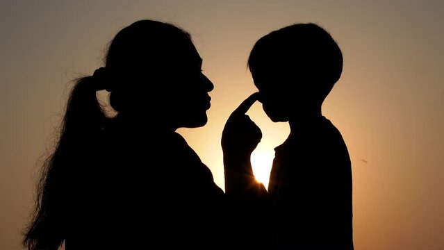 An Asian mother and her child share love in the evening at sunset. Silhouette view of a mom and kid having fun. A child with parents on holiday conceptual 4k video.