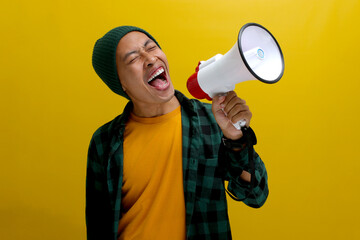 Excited Asian man in a beanie hat and casual shirt makes an announcement with a megaphone, using a...