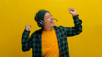 Young Asian man in a beanie and casual clothes dances with joy while listening to music on...