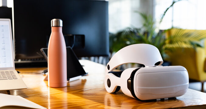 At office, VR headset resting on a wooden desk next to a laptop
