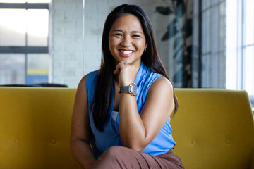 At office, biracial businesswoman wearing blue top, smiling at camera