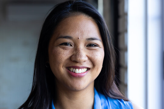 At office, biracial businesswoman in blue top stands near window