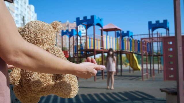 Ask child attention with toy. A man hands with teddy bear ask for child attention on the play ground.