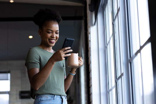 At office, African American businesswoman holding coffee, looking at phone, copy space