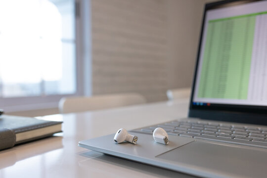 In the office, laptop shows spreadsheet; wireless earbuds rest on touchpad