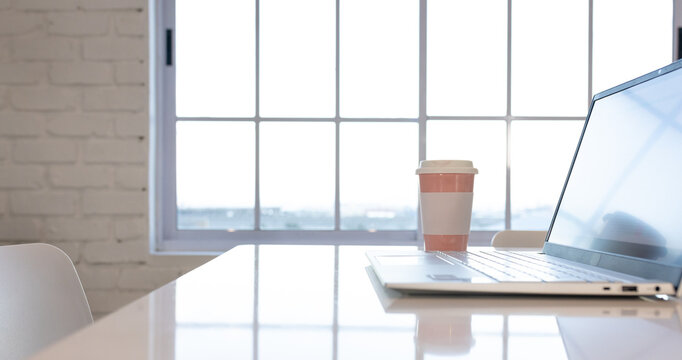 At office, laptop and coffee cup resting on white table near window