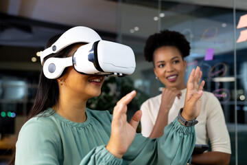 At office, diverse female colleagues wearing VR headsets working late