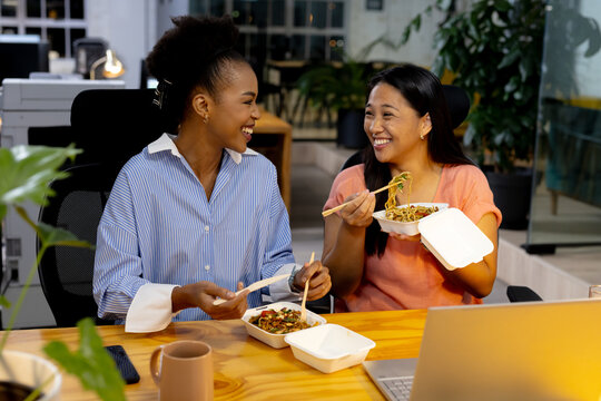 Diverse female colleagues enjoy a meal and work late at the office