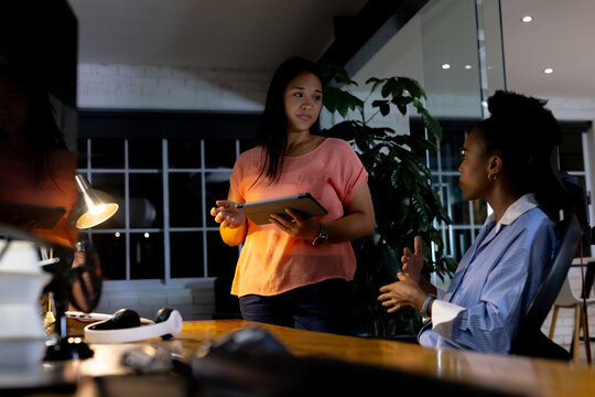 Diverse female business colleagues discussing work, holding tablet, working late - Powered by Adobe