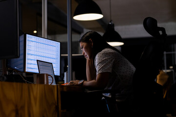 At office, biracial businesswoman examining sales tracker, working late
