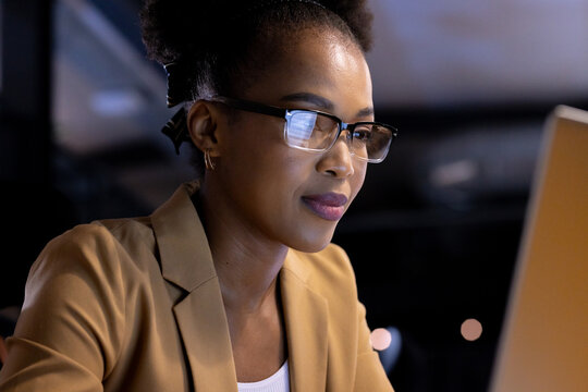 African American businesswoman in glasses focusing on computer screen, working late