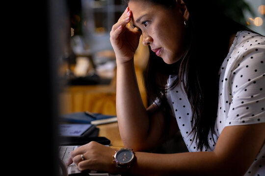 At office, biracial businesswoman examining business data graphics, working late