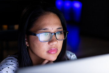 Biracial businesswoman in glasses works late, focusing on computer screen at office
