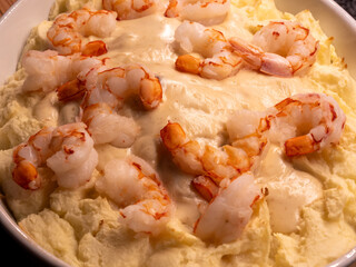 Seafood dinner in close-up in a white casserole dish with mashed potatoes, giant shrimps, white wine sauce and mashed potatoes.
