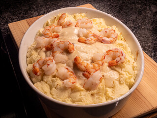 Seafood dinner in a white casserole dish with mashed potatoes, giant shrimps, white wine sauce and mashed potatoes, served on a wooden board.