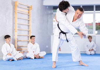 Male karate instructor training little child wearing kimono in dojo or jiu-jitsu in gym at tatami