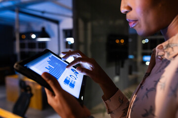 African American businesswoman reviewing data on tablet, working late