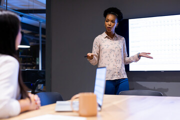 At office, diverse female colleagues discussing near sales tracker, working late