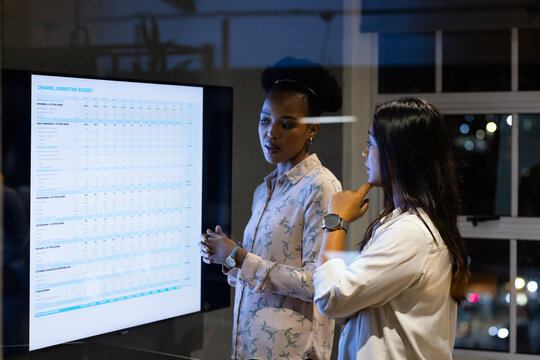 At office, diverse female colleagues examining sales tracker, working late