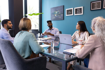 Diverse team discussing around table at office, senior African American man leading