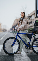 Obraz premium A fashionable young woman with headphones around her neck rides her bike on a city street, showcasing urban lifestyle and eco-friendly transportation.