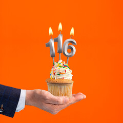 Hand holding birthday cupcake with number 116 candle - background orange