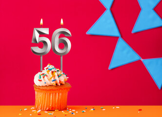 Number 56 candle with birthday cupcake on a red background with blue pennants