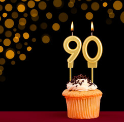 Number 90 birthday candle - Cupcake on black background with out of focus lights