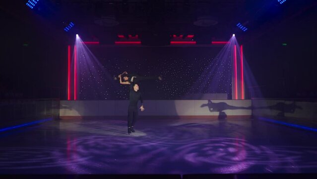 Figure skaters pair performs complex overhead lift, man holds woman parallel to ice on his outstretched arms, her legs in longitudinal split, then on one arm, rotating around. Clear silhouette of girl