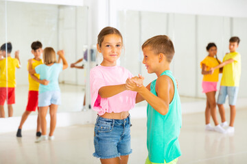 Positive preteen children learning to dance waltz in pairs in choreography class.
