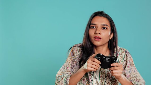 Jolly gamer celebrating after winning game on gaming console, studio background. Delighted Indian woman bragging after being victorious in videogame, defeating all enemies using gamepad, camera B