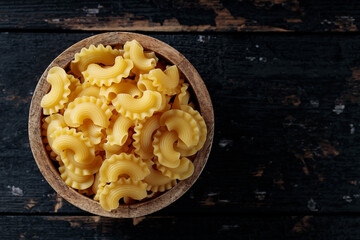 Raw Creste di Gallo Pasta in Wooden Bowl on Dark Vintage Background, Top View, Copy Space