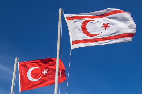 Turkey and Turkish Republic of Northern Cyprus flags waving in the blue and cloudy sky