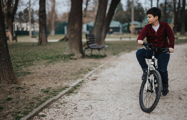 Active young kid on a bike, enjoying a joyful ride outdoors in a park setting surrounded by trees.