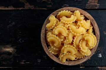 Raw Creste di Gallo Pasta in Wooden Bowl on Dark Vintage Background, Top View, Copy Space
