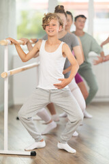 Obraz premium Positive teenage boy practicing plie position holding by ballet barre during choreography classes