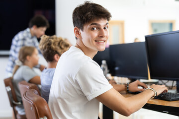 Young man working on computer together with other underage attendees of IT courses