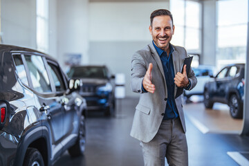 Good looking, cheerful and friendly salesman poses in a car salon or showroom. A professional car...
