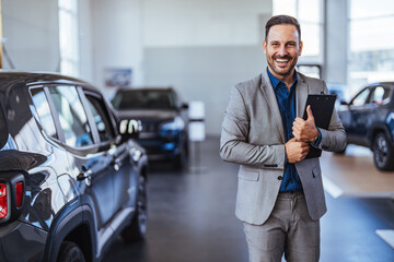 Salesperson at car dealership selling vehicles. Front view of handsome man standing in modern car...