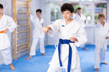 Diligent preteen attendee of karate classes practicing kata standing in row with others in sports...