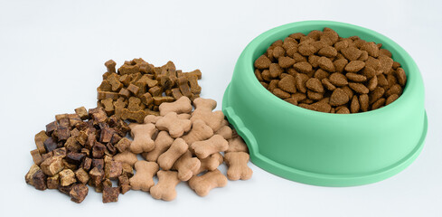 A full green bowl with dry food next to which there are dog treats in the form of bones. Dog food...