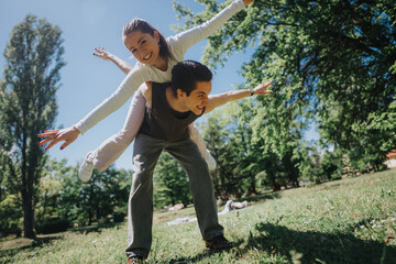 A cheerful couple having fun with a piggyback ride in the park, showing joy and playful...