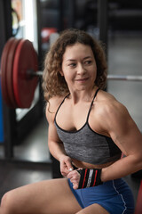 Caucasian forty-year-old woman puts on wrist straps before doing barbell exercises in the gym....
