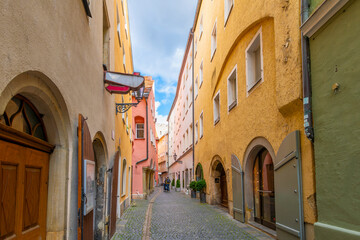 Obraz premium A colorful narrow cobblestone alley full of shops and businesses in the historic medieval altstadt district of the Bavarian city of Regensburg, Germany.