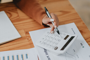 Close-up view of a business professional's hand using a calculator over financial charts and data,...