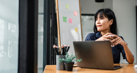 Professional woman pauses at her workplace, looking away from her laptop, possibly brainstorming or problem-solving.