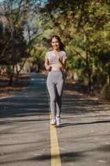 Cheerful young woman in fitted athletic wear enjoys a solitary run on a sun-dappled path through the woods.