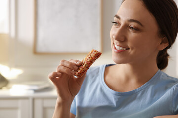 Woman holding tasty granola bar at home