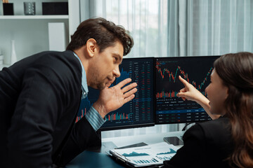 Two business traders discussing on dynamic stock market in currency rate investment trading on two pc screens with compare real time graph on risk or profit point of data at modern office. Postulate.